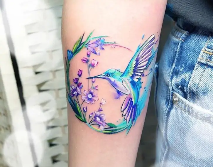 circle with flowers and hummingbird watercolor tattoo on forearm
