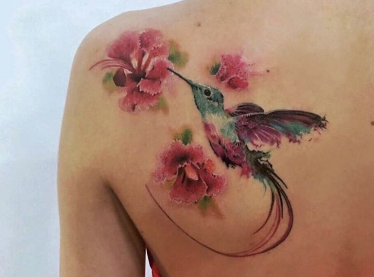 colorful hummingbird in flowers with subtle and vivid colors tattoo on the back