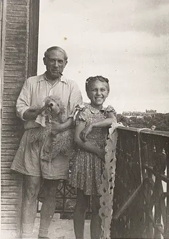 Pablo Picasso standing in the balcony a kid while carrying his poodle