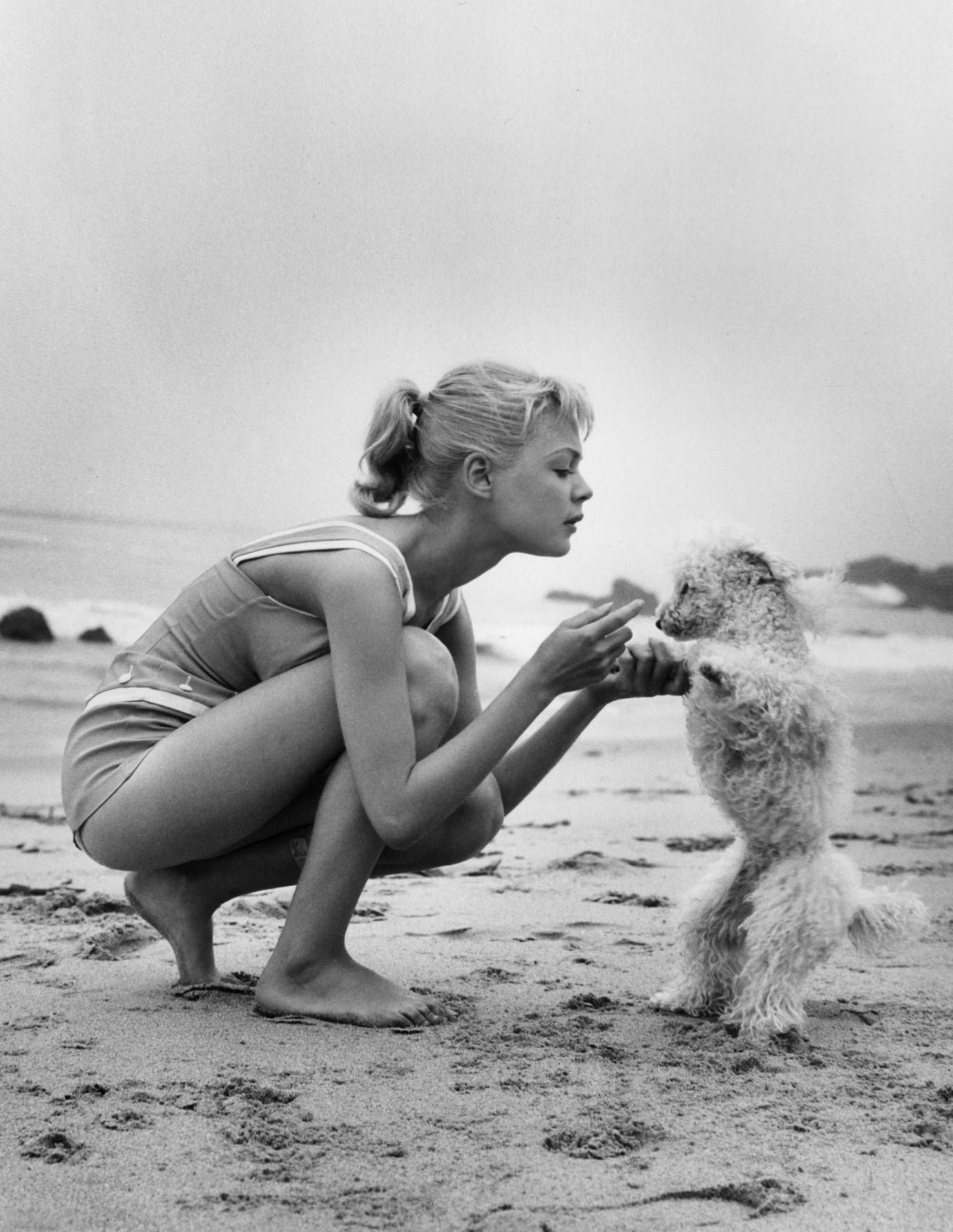  Sandra Dee at the beach holding the arms of her poodle standing up in front of her