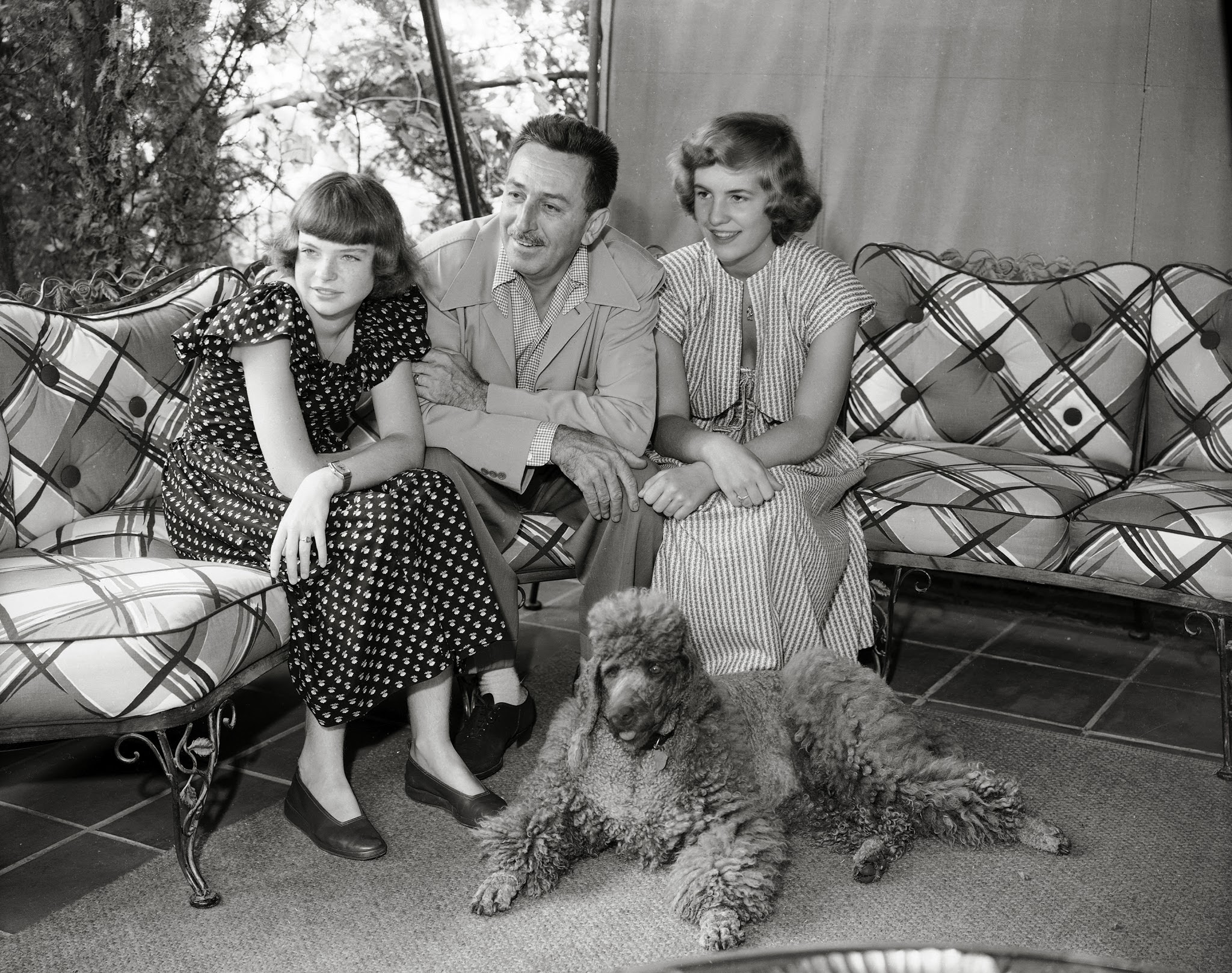 Walt Disney sitting on the couch with his family and their poodle lying on the floor next to their feet