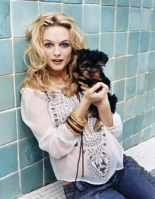 Heather Graham sitting on the floor leaning on a wall while holding her Schnauzer puppy