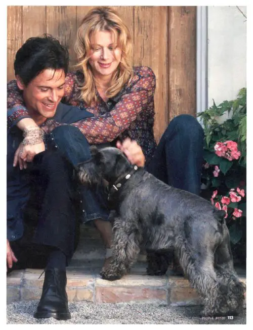 Rob Lowe sitting on the stairs while petting his Schnauzer standing in front of him