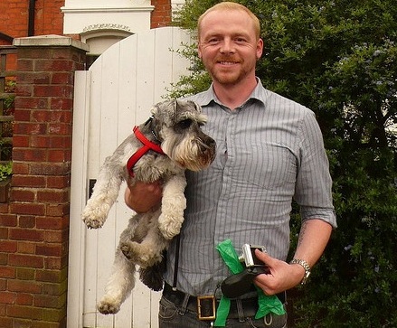 Simon Pegg holding his Schnauzer while standing in front of a house