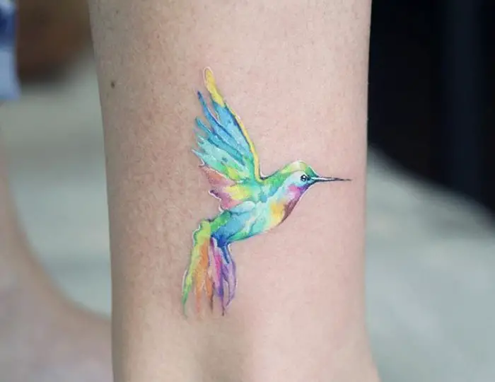 small pastel colored watercolor hummingbird tattoo on the leg