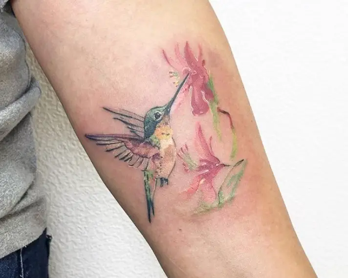 hummingbird feeding on flowers watercolor tattoo on the forearm