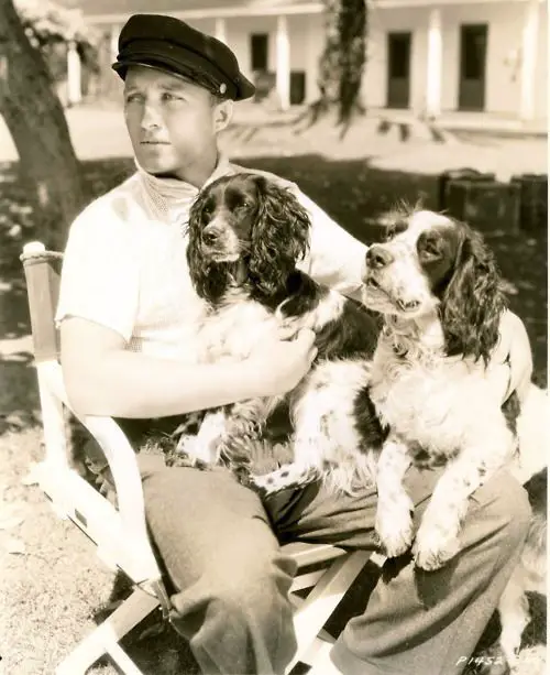 Bing Crosby sitting on the chair outdoors with his two Cocker Spaniels in his lap