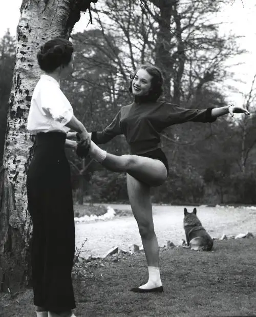 Julie Andrews stretching while her Corgi is sitting by the road