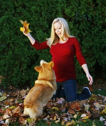 Kendra Wilkinson kneeling on the dried leaves in front of the Corgi dog while holding up a bunch of dried leaves