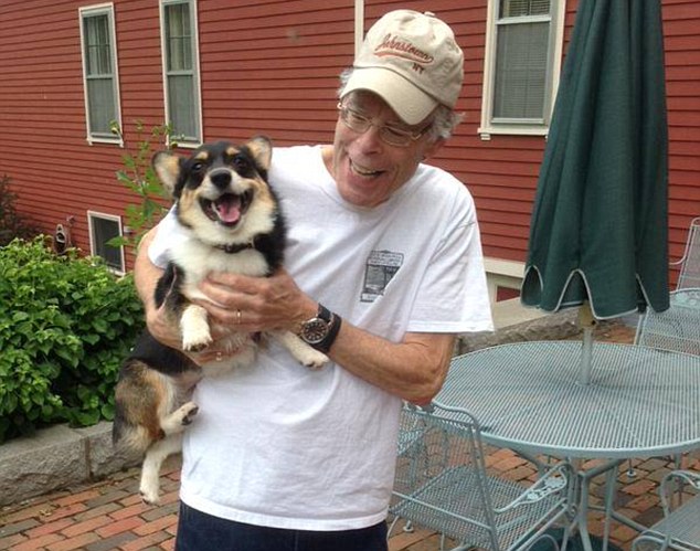 Stephen King standing in the patio while carrying his smiling Corgi