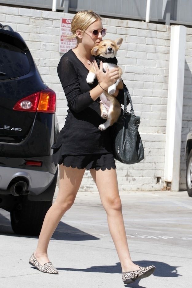 Tallulah Willis walking in the parking lot while carrying her Corgi under the sun