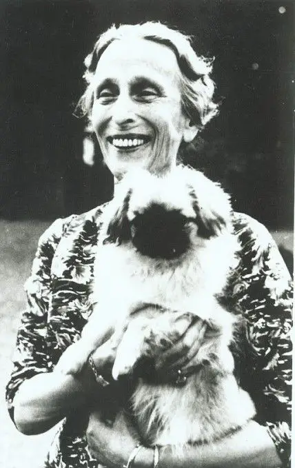 Queen Louise of Sweden, second wife of King Gustaf VI Adolf of Sweden. holding her Pekingese while smiling