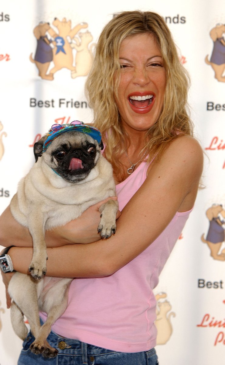 Tori Spelling excitedly smiling while carrying her Pug