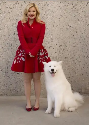 Kelly Clarkson in red dress and sandals with her Samoyed Dog sitting on the floor