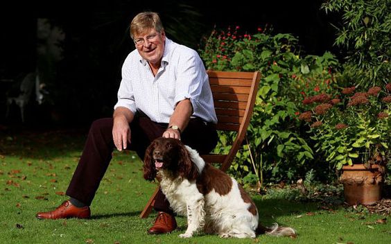 Ed Stourton sitting on the chair in the garden while petting his Springer Spaniel sitting on the grass