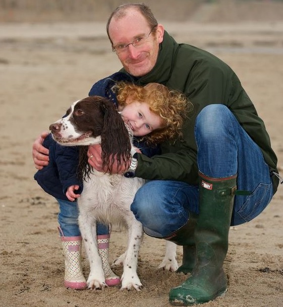 Richard Dale hugging his Springer Spaniel together with his child at the beach