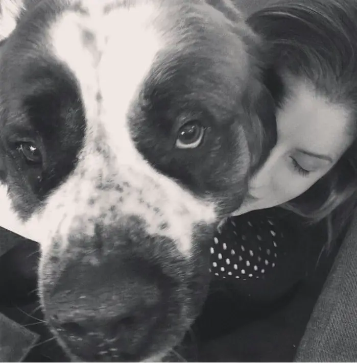 black and white photo of Anna Kendrick hugging her St. Bernard Dog from behind 