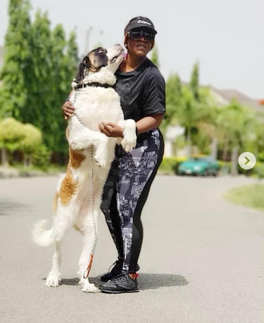Empress Njamah behind her St. Bernard Dog supporting her from standing up while licking her face