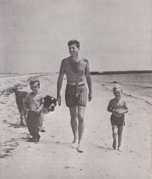 an old photo of John Kennedy walking by the seashore with his two kids and their St. Bernard Dog walking behind them