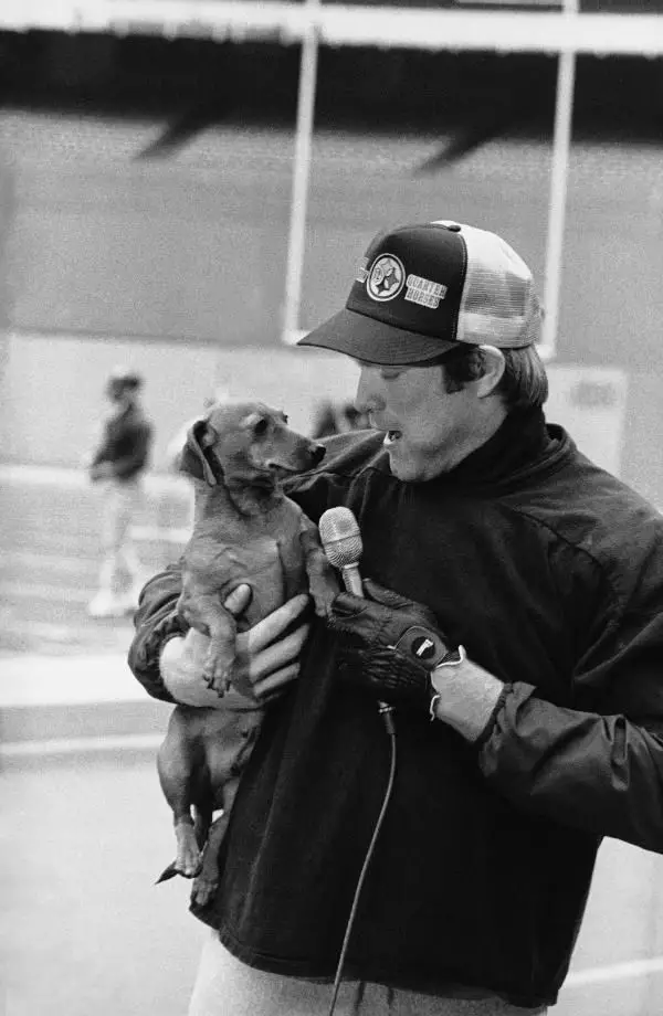 black and white photo of Terry Bradshaw carrying his dachshund dog