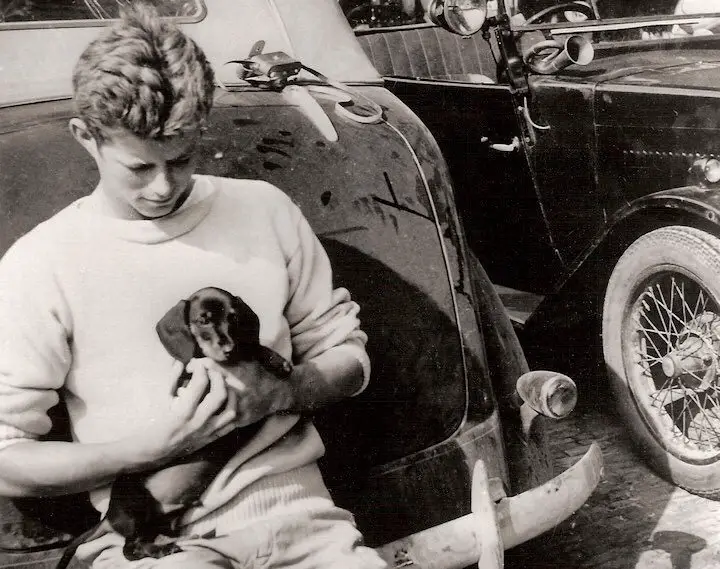 JFK sitting on the back of the car while holding his Dachshund