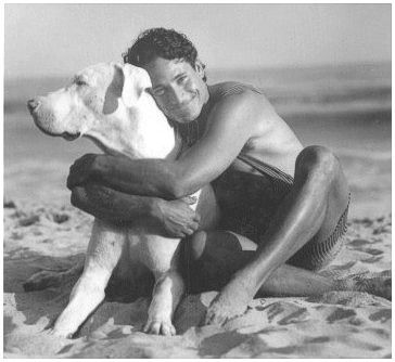 Greg Louganis sitting in the sand while hugging his Great Dane