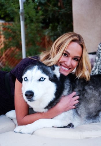 Ashlan Gorse lying on the couch outdoors while hugging her Husky