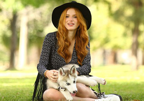 Bella Thorne sitting on the grass with her Husky puppy lying on her lap