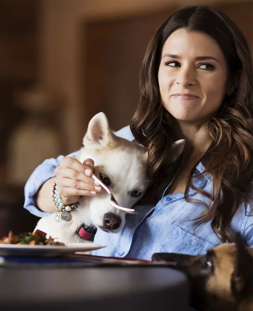 Danica Sue Patrick with her Husky puppy in between her arms staring at the fork in her hand