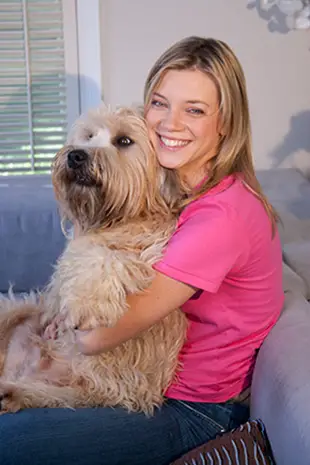 Amy Smart sitting on the couch while hugging her Labradoodle