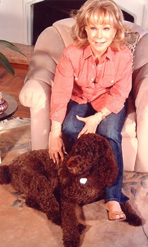 Barbara Eden sitting on the couch while petting her Labradoodle on the floor