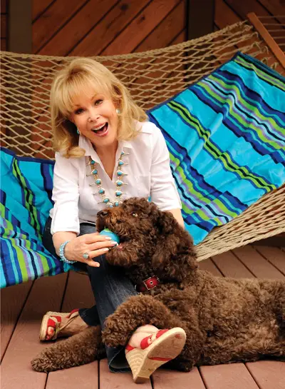 Barbara Eden sitting in a hammok while getting the ball from her Labradoodle mouth