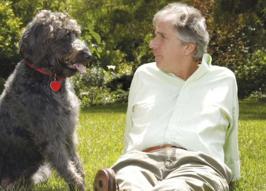 Henry Winkler sitting on the grass with his Labradoodle on his side