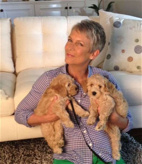 Jamie Lee Curtis sitting on the floor while holding her two Labradoodle puppies