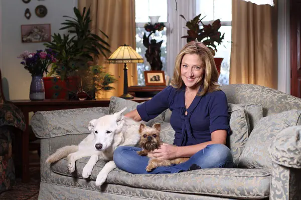 Marley (Edie Falco) sitting on the couch while petting her cream labrador and yorkie