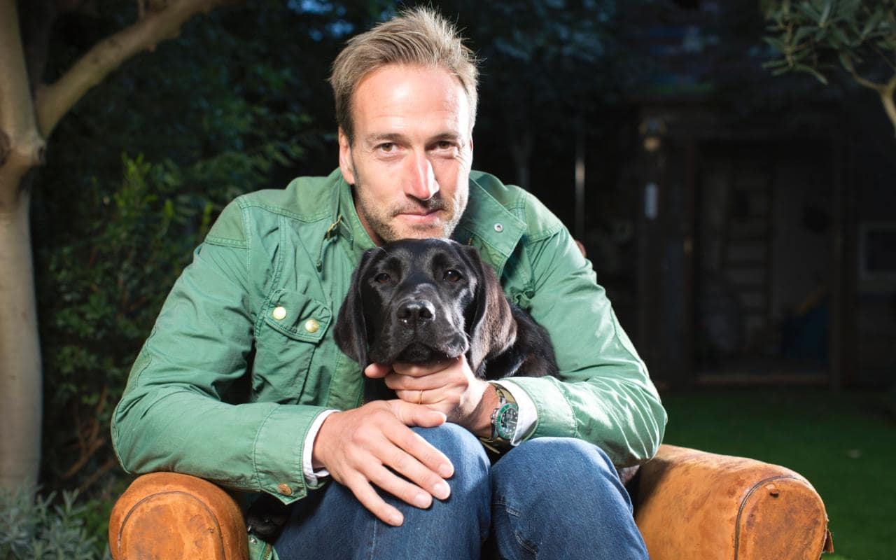 Ben Fogle sitting on the couch with his black Labrador in his lap