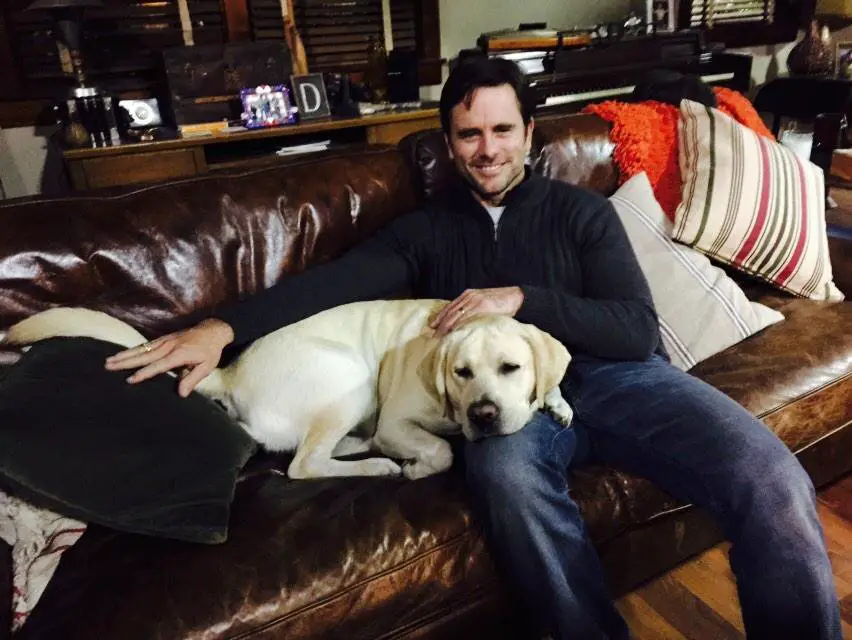 Charles Esten sitting on the couch while his Labrador is lying beside beside him with its head on his lap