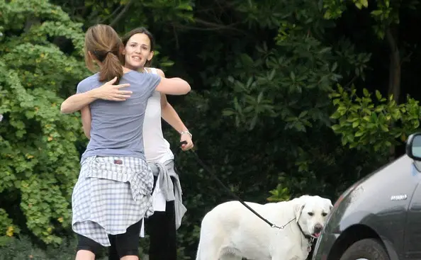 Jennifer Garner hugging her lady friend while holding the leash of her Labrador standing in front of the car