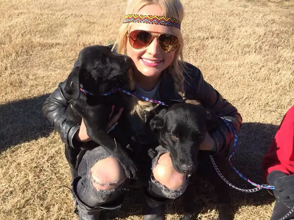 Miranda Lambert sitting on the grass with her two black Labrador puppies in her lap