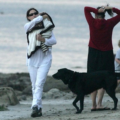 Minnie Driver walking by the beach while carrying her baby and her Labrador Retriever is walking towards her
