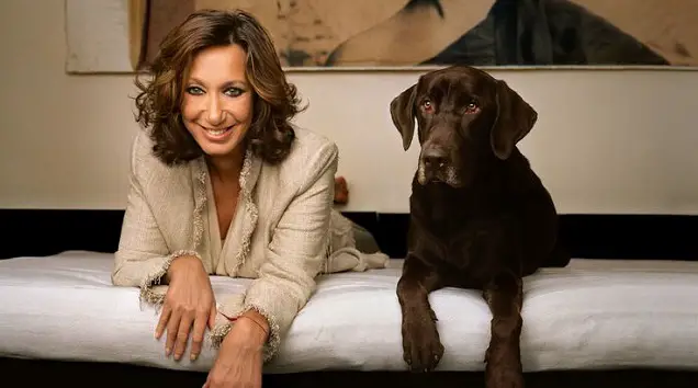 Donna Karan lying down on the bed next to her Chocolate brown Labrador Retriever