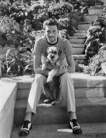 black and white photo of Laurence Olivier sitting in the garden with his Schnauzer in his lap