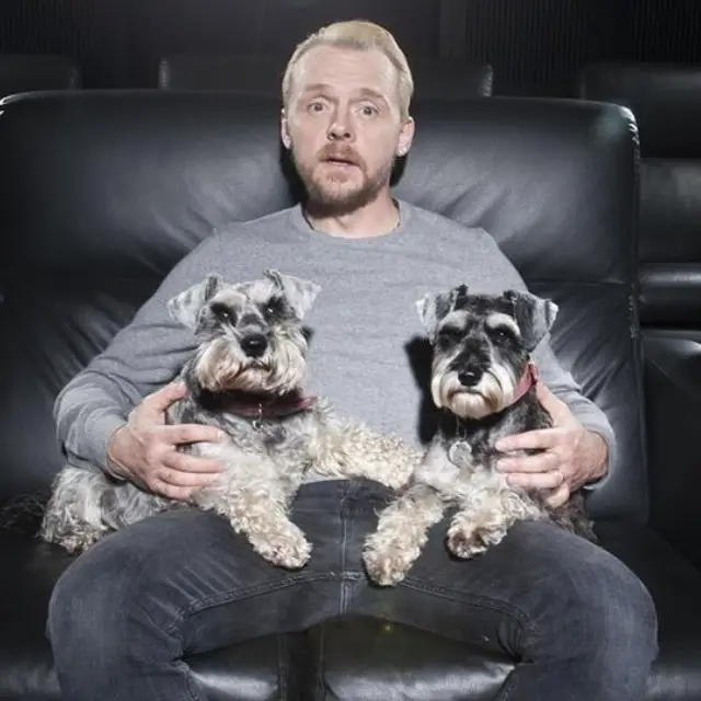 Simon Pegg siting on the couch with his two Schnauzers