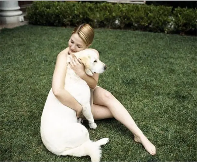 Drew Barrymore sitting in the lawn while hugging her Labrador