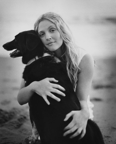 black and white photo of Drew Barrymore at the beach hugging her Labrador