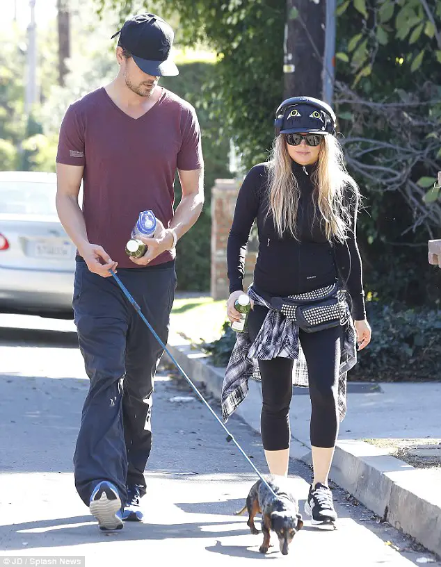 Fergie and Josh walking in the street with their Dachshund on a leash
