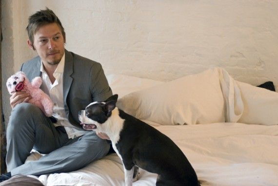 Norman Reedus sitting on the side of the bed with a Boston Terrier