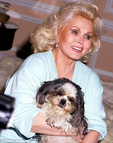 Zsa Zsa Gabor sitting on the bed with her Shih Tzu on her lap