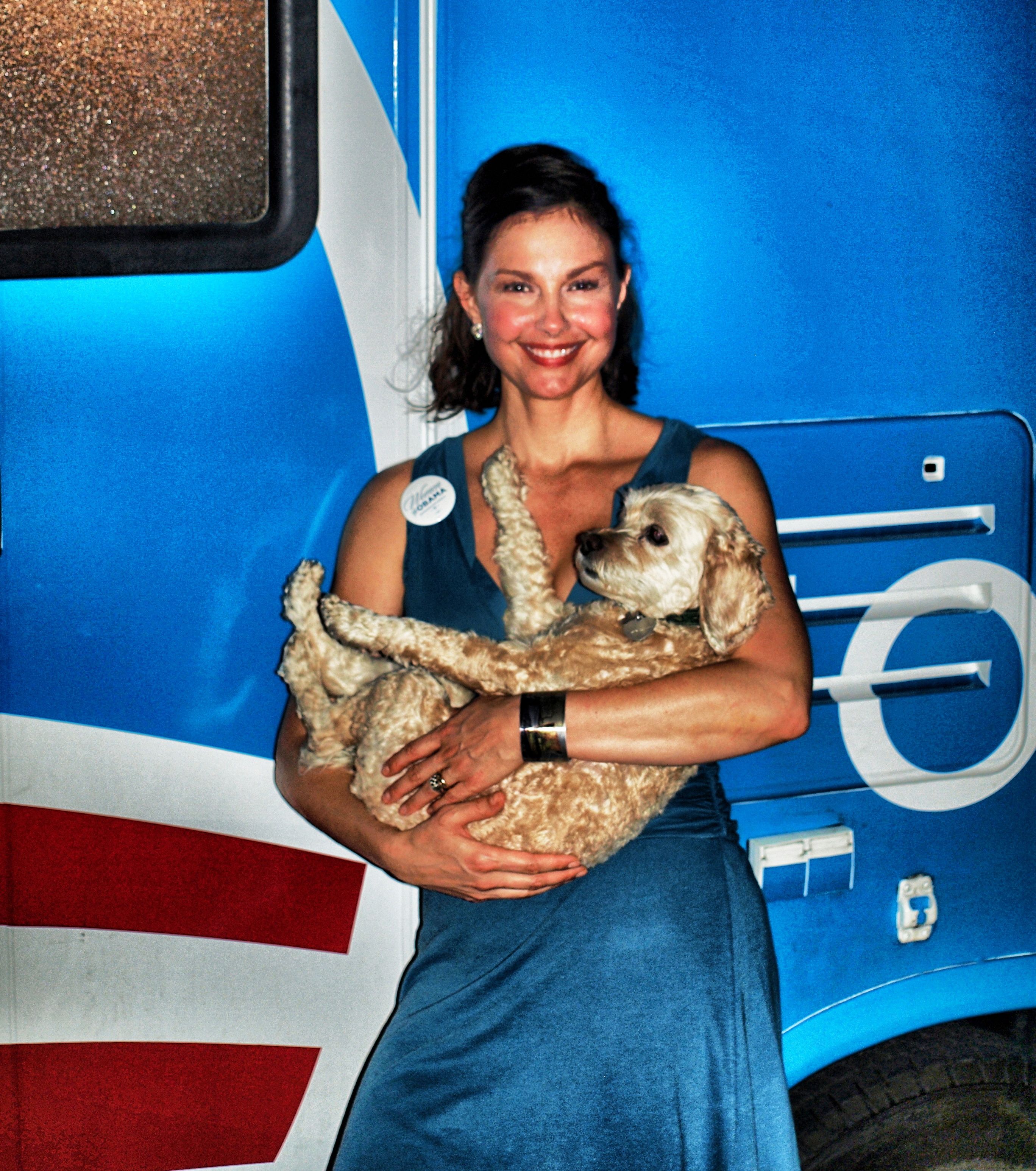 Ashley Judd standing in front of a bus while carrying her Cocker Spaniel
