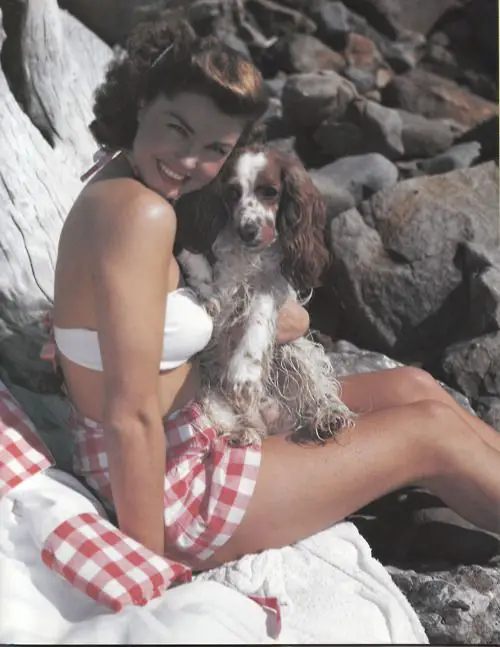 Esther Williams sitting on a towel placed on the rocks with her Cocker Spaniel
